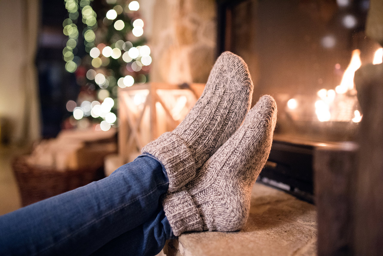 Feet of unrecognizable woman in woollen socks by the Christmas fireplace