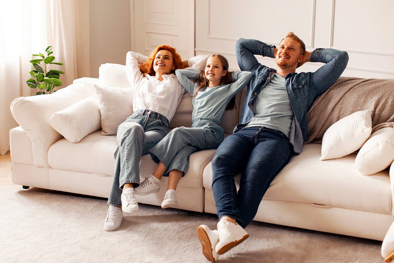 Cheerful family with child girl enjoying quality time at home in their living room, sitting on comfortable sofa, smiling and looking relaxed stock photo